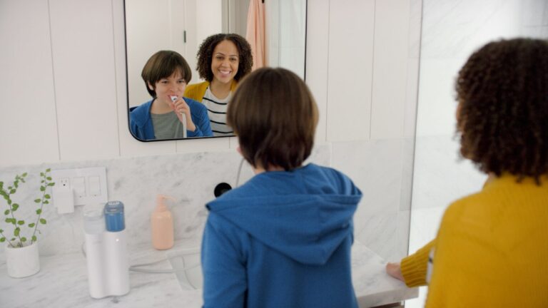 Parent and child brushing teeth together beside several unbranded toothpaste tubes.